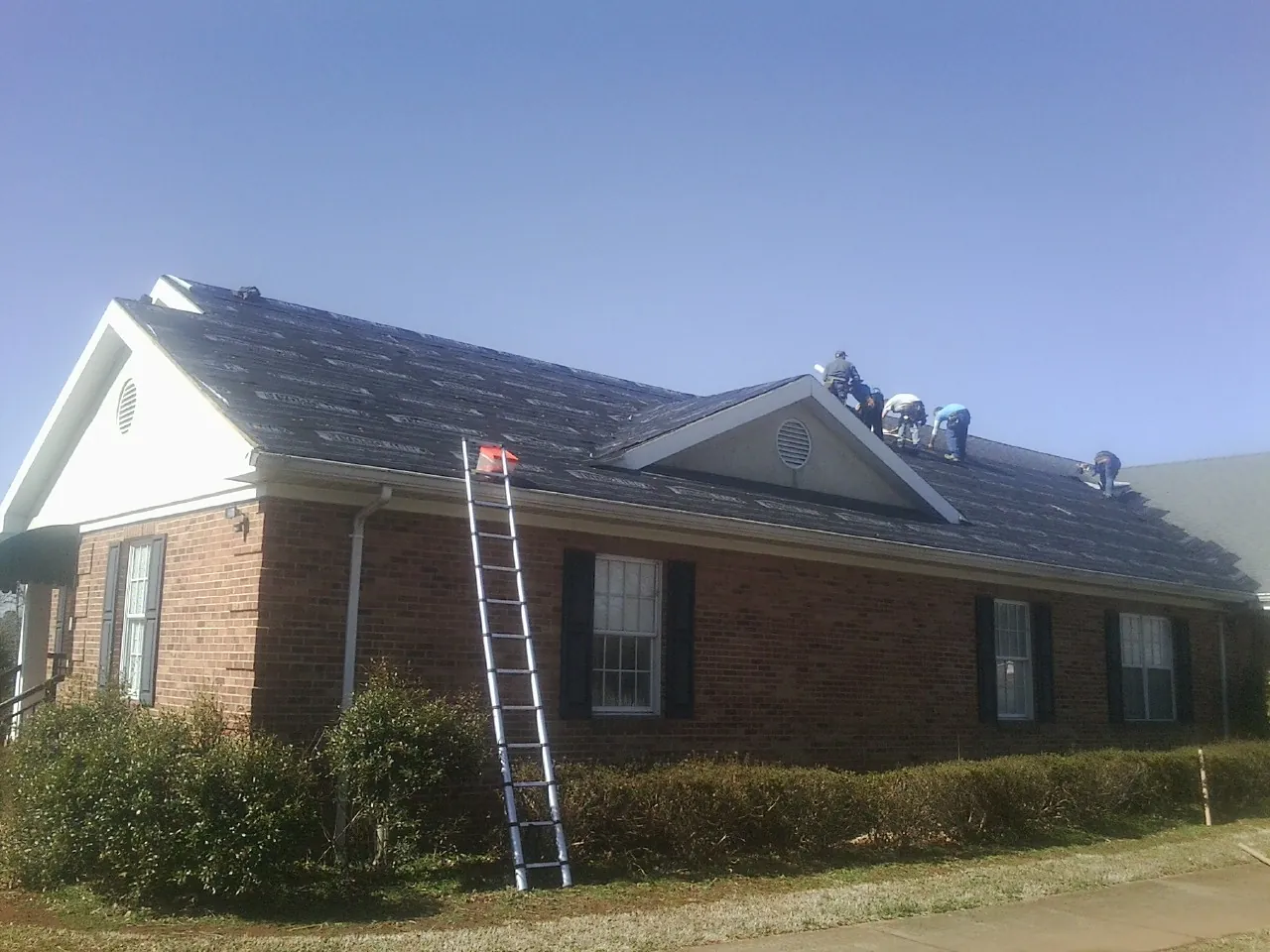 Crew tearing shingles off a brick ranch roof with a ladder set — Metal Roof Repair work by our crew in Bybee