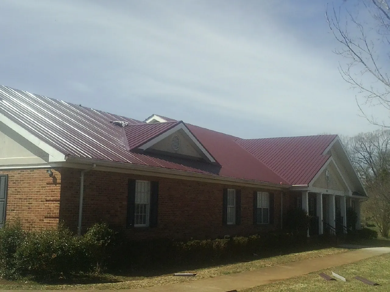 Red metal roof with gabled entries on a long brick building, from a Hail Damage Roof Repair job in Bybee