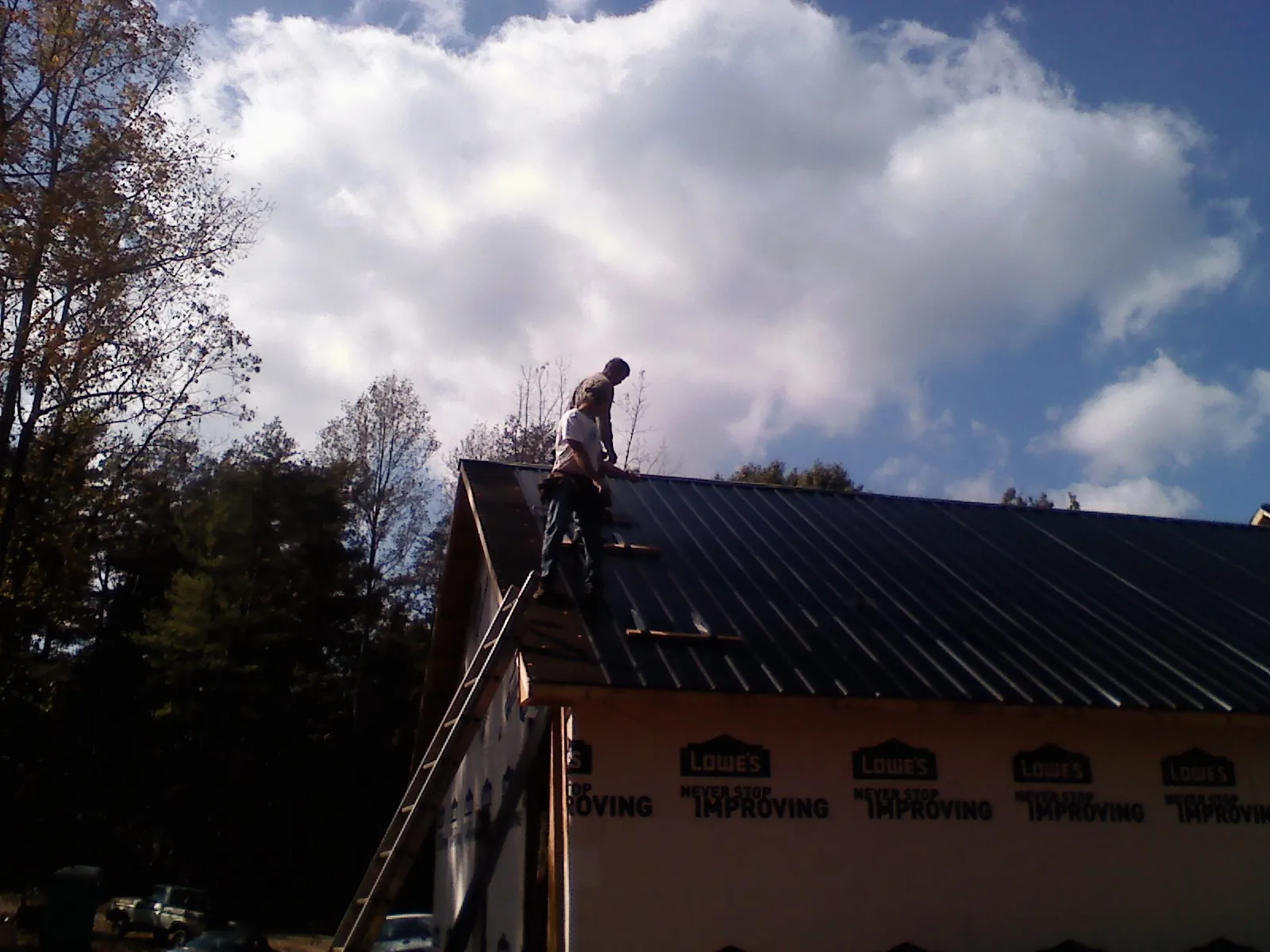 Roofer fastening dark metal panels high against a cloudy sky, from a Roof Inspection job in Bybee