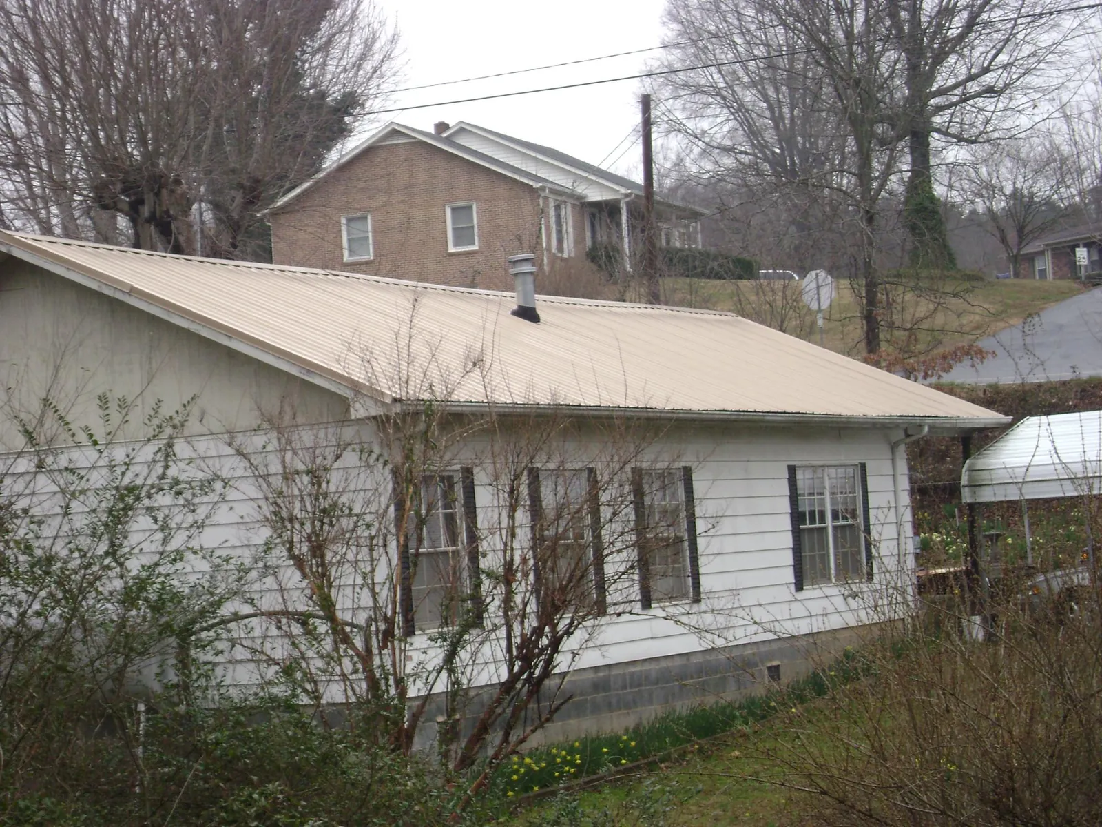 Tan metal roof on a white sided house set into a hillside — Commercial Roofing by Roofing Brothers in Bybee